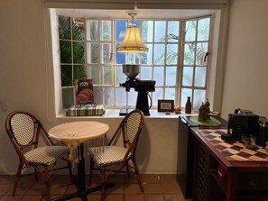 Una habitación acogedora con ventanal, una mesa con sillas, una cámara antigua y un tablero de ajedrez.