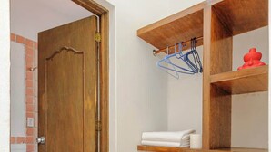 Una habitación con puerta de madera, suelo de baldosas y estantes de madera con toallas y un perchero azul.