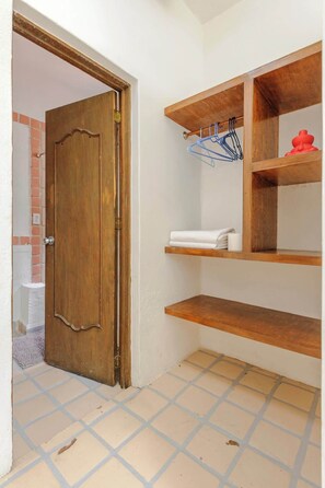 Una habitación con puerta de madera, suelo de baldosas y estantes de madera con toallas y un perchero azul.
