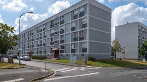 Ein modernes, mehrgeschossiges Gebäude mit einer flachen Fassade, großen Fenstern und einem gut sichtbaren Eingang mit roter Markise.