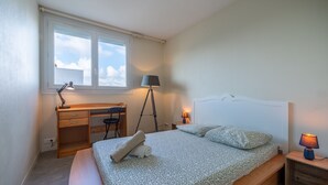 Ein Schlafzimmer mit Bett, Schreibtisch, Stuhl, Lampe und Fenster.