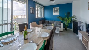 Ein Essbereich mit Tisch für vier Personen, einer Couch und einem Balkon mit Blick auf Gebäude.