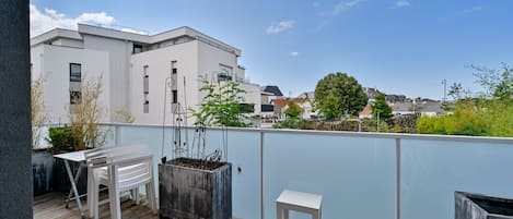 A balcony with a white table and chair, a potted plant, and a small stool.