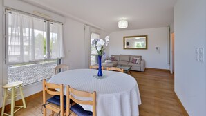 A dining area with a round table, chairs, and a vase of flowers. There is a sofa and a mirror in the background.