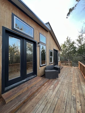 A modern house with large sliding glass doors, a wooden deck, and a built-in seating area. - Cozy Cottage Retreat in Nature (Cedar Creek)