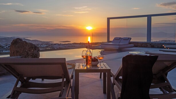 Zonsondergang vanaf een terras met een tafel, twee stoelen en een fles wijn.