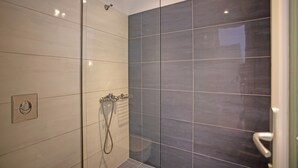 Een moderne douchecel met glazen deur, betegelde wanden en een zichtbare douchekop.