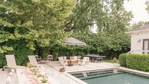 Un área junto a la piscina con sillones reclinables, una mesa de comedor decorada con flores y una guirnalda de luces.