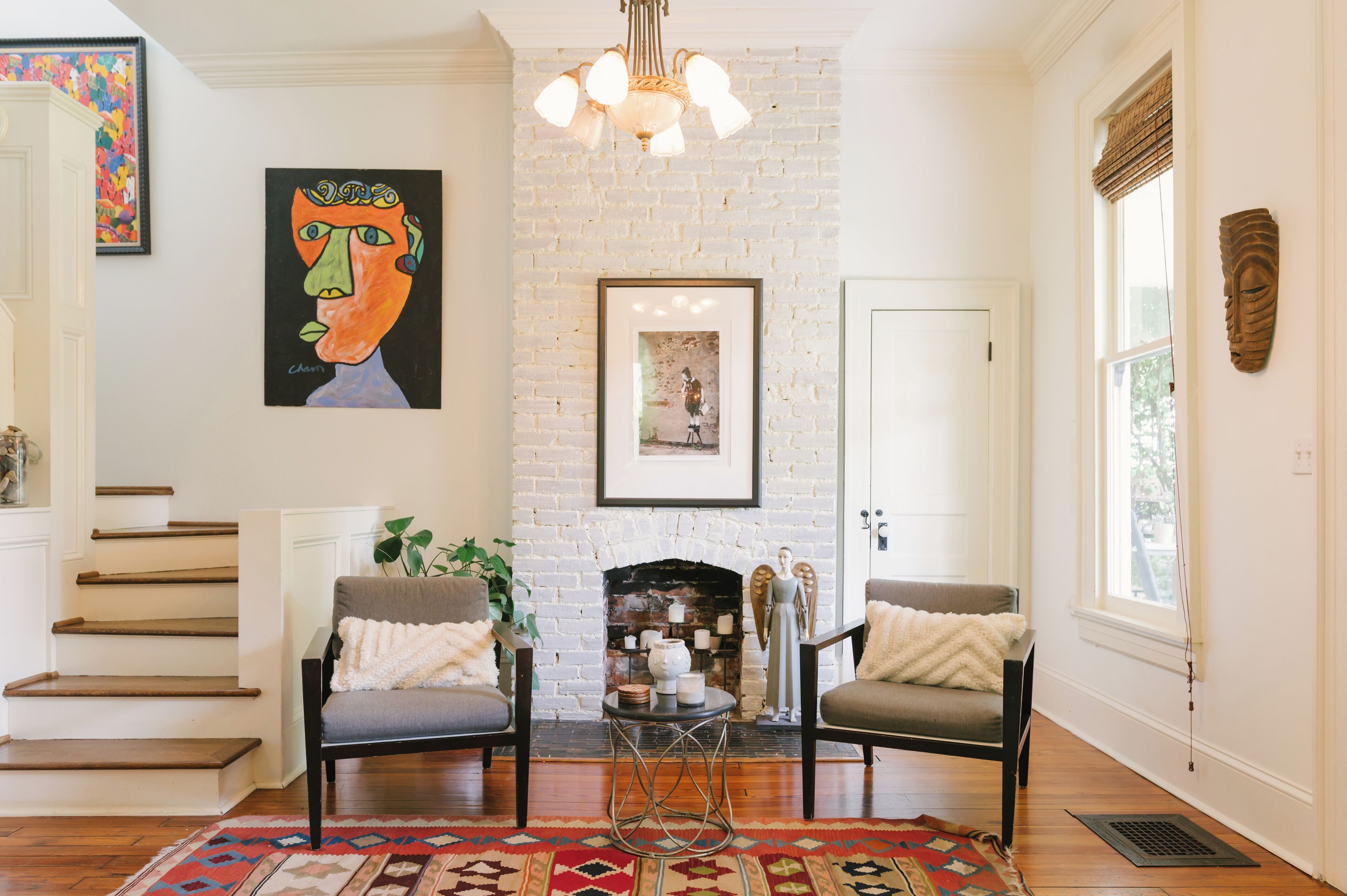A living room with a white brick fireplace, two armchairs, a coffee table, and a staircase.