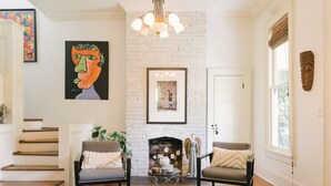 Una sala de estar con chimenea de ladrillo blanco, dos sillones, una mesa de centro y una escalera.
