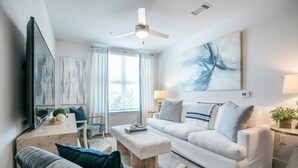 A modern living room with a white sofa, a coffee table, and a TV. - The Jackson, 2BR Luxe Condo by Velvet Ditch Villas (Oxford)