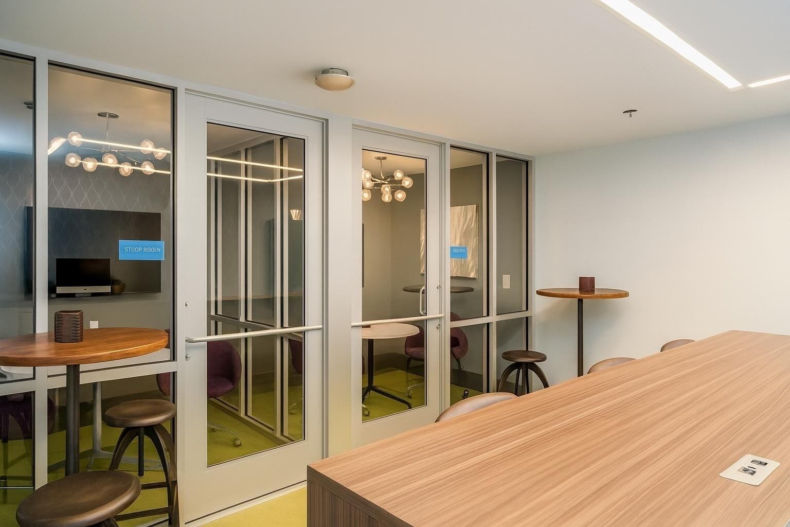 A conference room with a long table, stools, a television, and glass partitions.