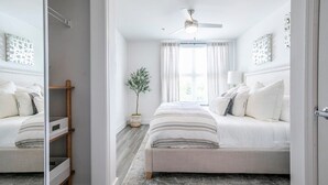 A bedroom with a bed, a ceiling fan, a window with curtains, and a plant. - The Jackson, 2BR Luxe Condo by Velvet Ditch Villas (Oxford)