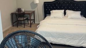 Une chambre à coucher comprenant un lit, un bureau, une chaise, une lampe et un ventilateur sur pied.