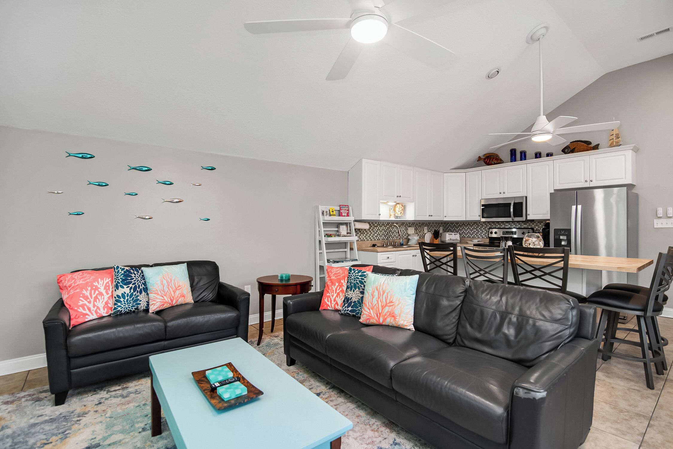 A modern living room with two black leather sofas, a light blue coffee table, and a ceiling fan.
