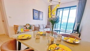 Uma sala de jantar com uma mesa posta para dois, um sofá ao fundo e uma janela grande com vista.