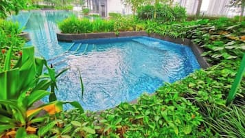 A swimming pool surrounded by lush greenery and modern buildings in the background.