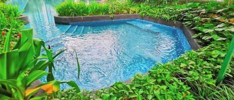 A swimming pool surrounded by lush greenery and modern buildings in the background.