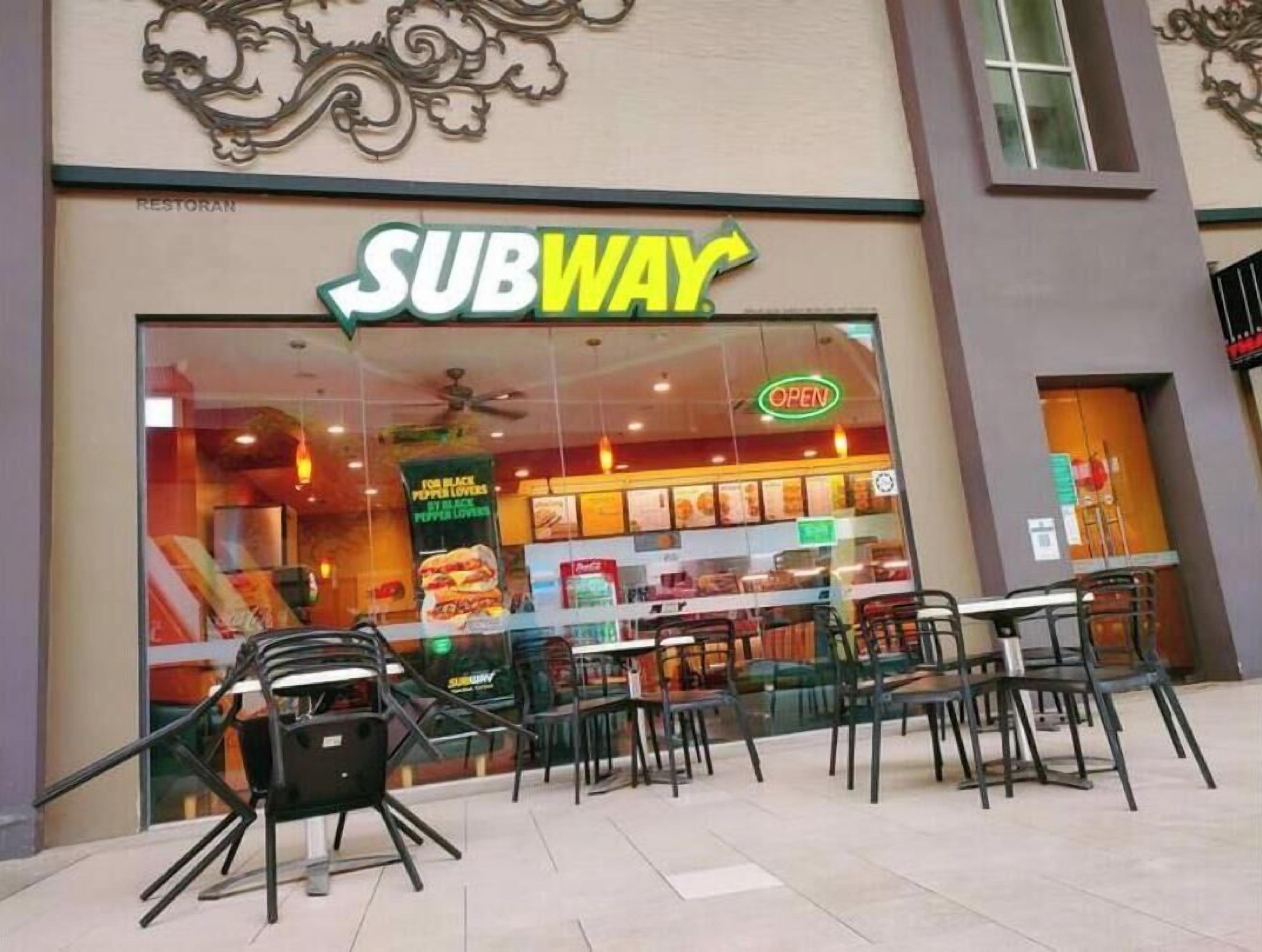 Un ristorante SUBWAY con facciata in vetro, area salotto all'aperto e insegna luminosa 'OPEN'.