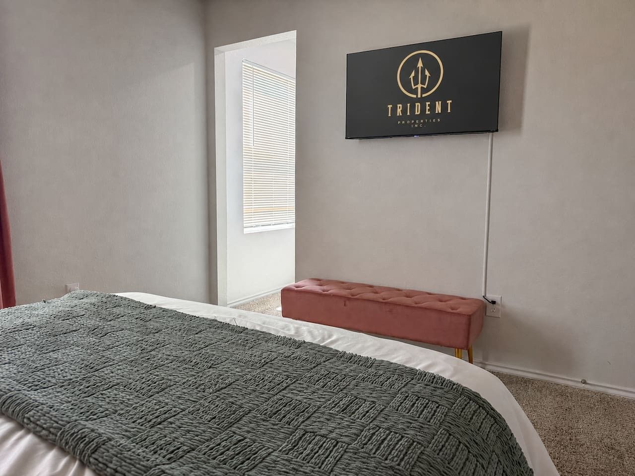 A bedroom with a bed, a bench, a window with blinds, and a wall-mounted sign.