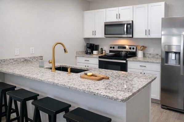 A modern kitchen with white cabinets, a stainless steel refrigerator, a black stove, and a granite countertop.