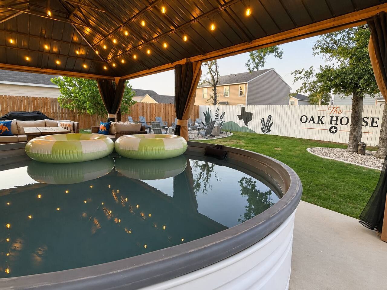 Un área de jacuzzi al aire libre con techo cubierto, sillas de descanso y cerco de madera identificado como 'The Oak House'.