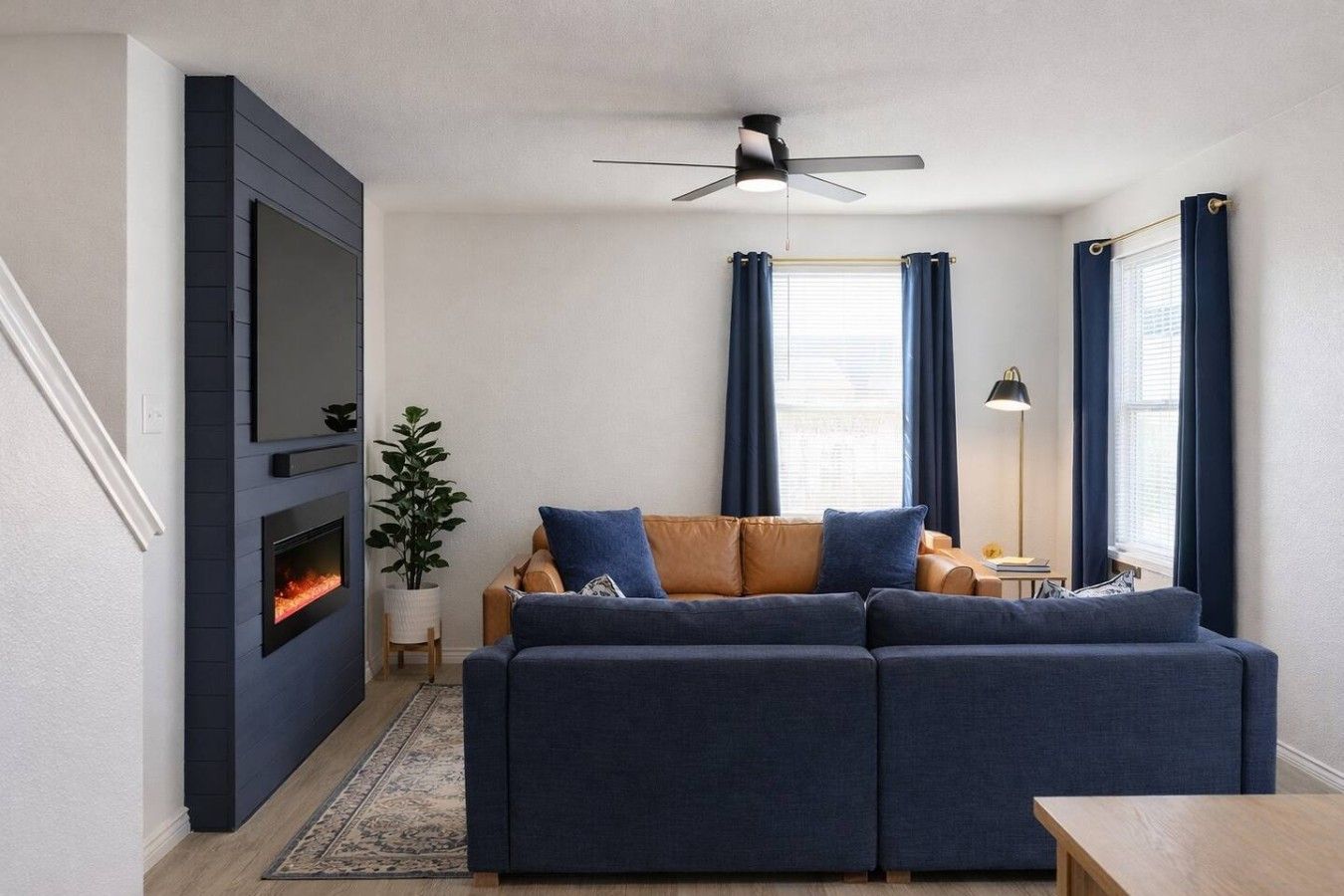 A living room with a fireplace, a sofa, a ceiling fan, and a window with curtains.