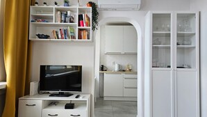 A modern living room with a flat-screen TV, white cabinetry, a bookshelf, and a kitchen area with white cabinets. - Downtown Apt - Top Location, Metro nearby (Warszawa)