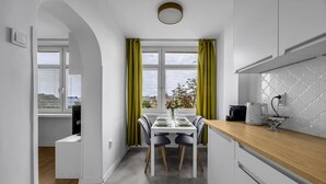 A modern kitchen with a wooden countertop, a dining area with a table and chairs, and a view through large windows with green curtains. - Downtown Apt - Top Location, Metro nearby (Warszawa)
