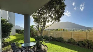 Un patio con una mesa y sillas, un árbol pequeño y vistas a la montaña.