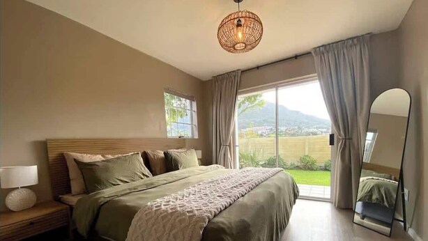 Un dormitorio con una cama grande, una mesita de noche con lámpara, una ventana con cortinas y vistas al exterior.