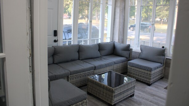 A sunroom with a grey sectional sofa, wicker chairs, and a glass coffee table. - Spacious, Fully Remodel 4-bedroom house 2.5 bathroom in charming Carthage (Carthage)