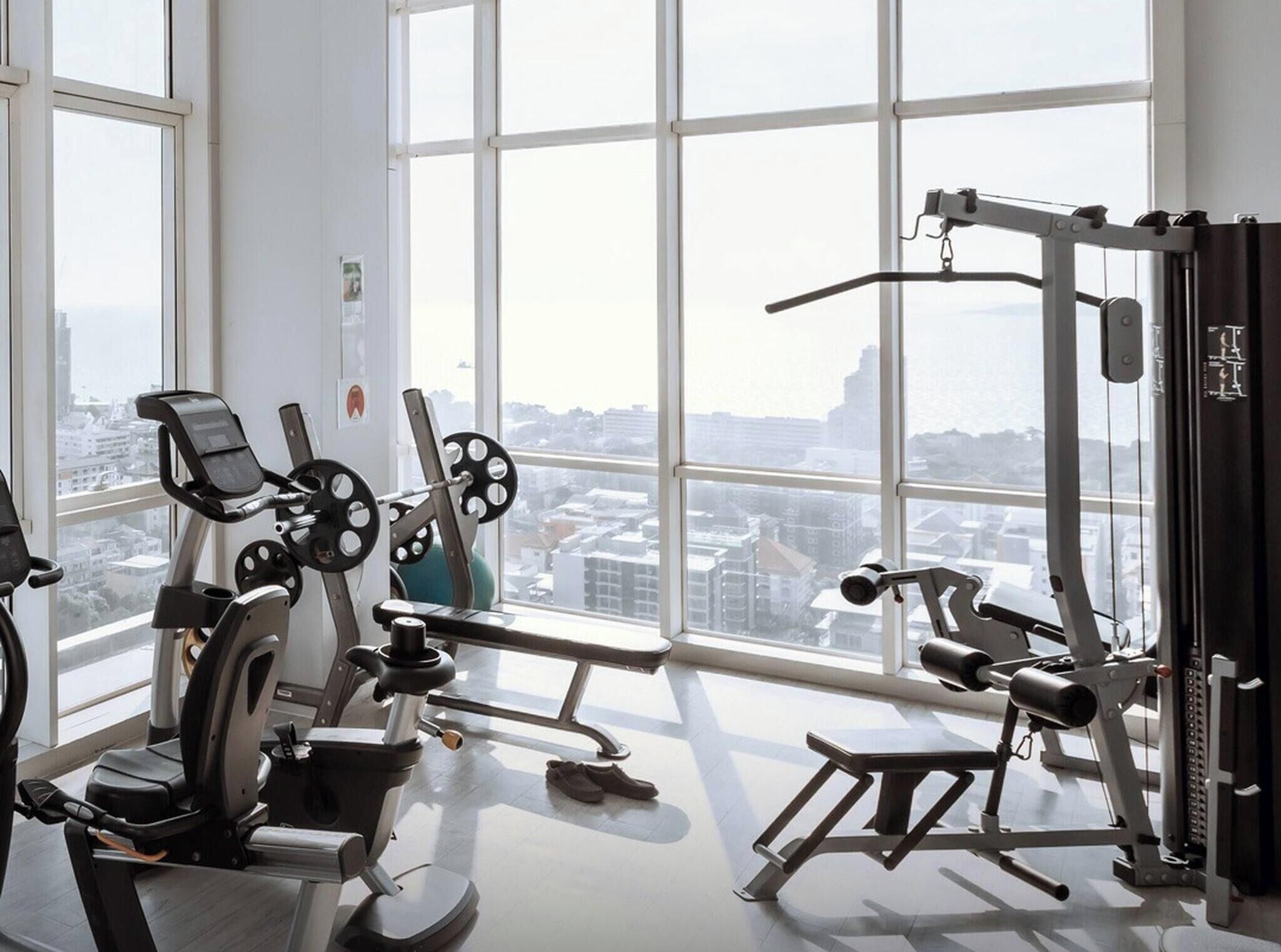 A gym with various exercise equipment, large windows, and a view of a cityscape.
