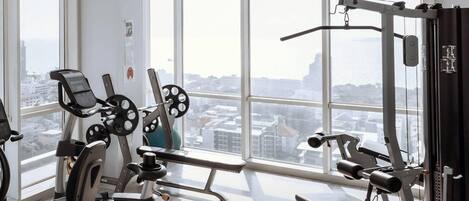 A gym with various exercise equipment, large windows, and a view of a cityscape.