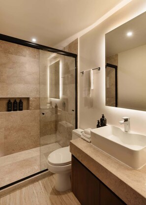Un baño moderno con ducha envuelta en vidrio, inodoro blanco, espejo grande y encimera color beige.