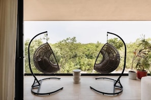 A balcony with two wicker chairs and a small table, overlooking a lush green landscape.