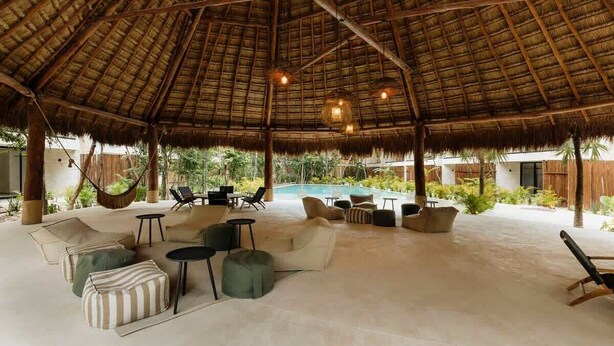 An open-air lounge with a thatched roof, outdoor seating, and a pool in the background. - Soluna Samsara Jungle Retreat Beach Club Access (Tulum)