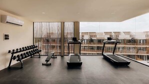A gym with treadmills, a bench, and dumbbells, with a view of buildings through large windows. - Soluna Samsara Jungle Retreat Beach Club Access (Tulum)