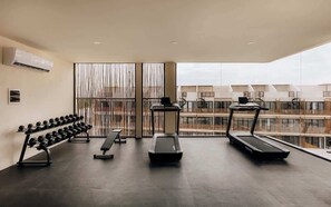 A gym with treadmills, a bench, and dumbbells, with a view of buildings through large windows.
