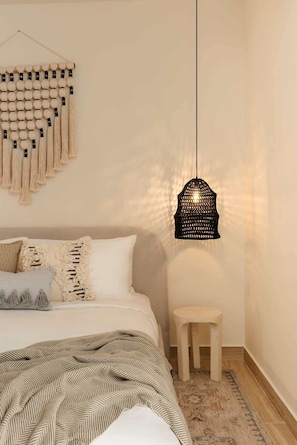 A bedroom with a bed, a hanging wall decoration, a small stool, and a hanging light fixture.