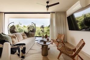 A modern living room with a sofa, two wicker chairs, a round coffee table, and a ceiling fan.