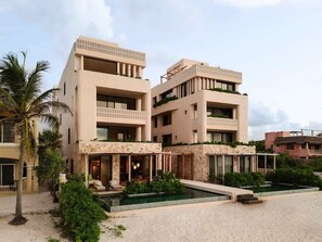 Un hĂŽtel moderne Ă plusieurs Ă©tages, dotĂ© dâune piscine, dâun espace extĂ©rieur amĂ©nagĂ© et offrant une vue sur la plage.