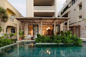 Zona junto a la piscina con un espacio de descanso cubierto, piscina y un edificio con balcones.