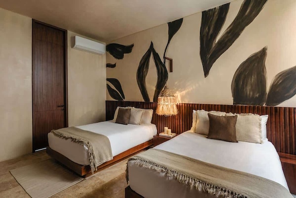 A hotel room with two beds, a wooden headboard, a wall-mounted air conditioner, and a textured wall decoration.