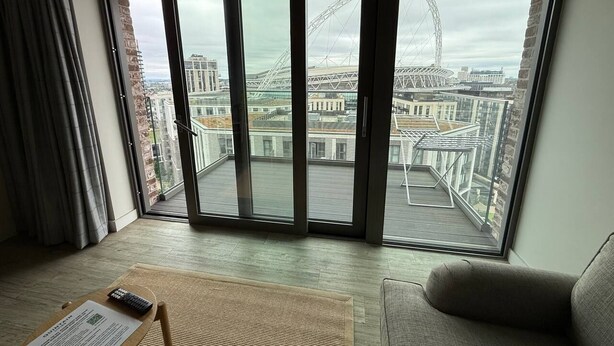 Una habitación con un amplio ventanal corredera que da a un balcón con vistas a una noria y al paisaje urbano.