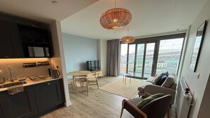 Una sala de estar moderna con un sofá, una mesa de comedor con sillas y una cocina con armarios oscuros y un microondas.