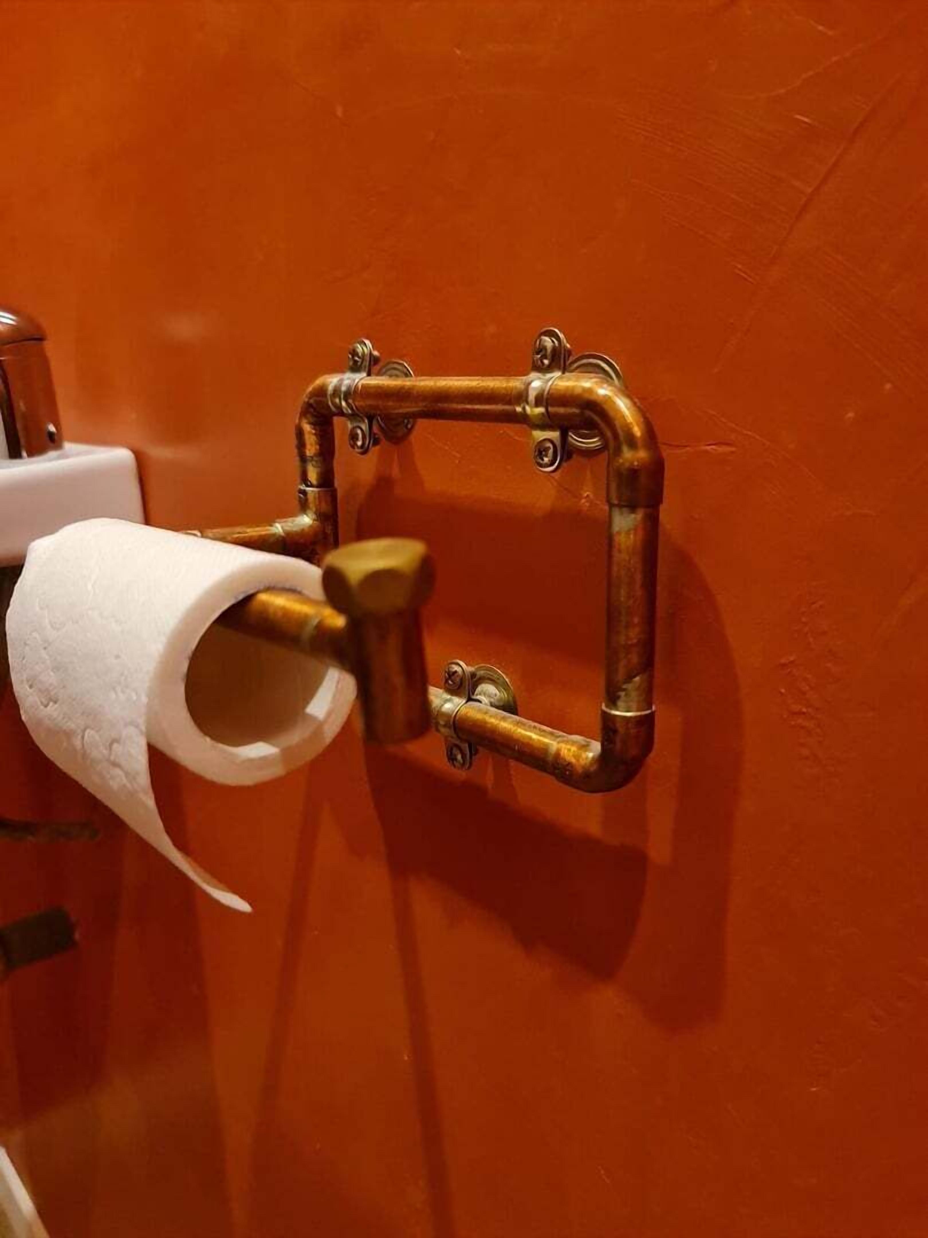 Un porte-rouleau de papier toilette fixé au mur, doté d’un cadre métallique carré.
