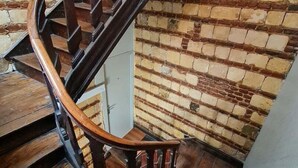 A wooden spiral staircase with a brick wall background.