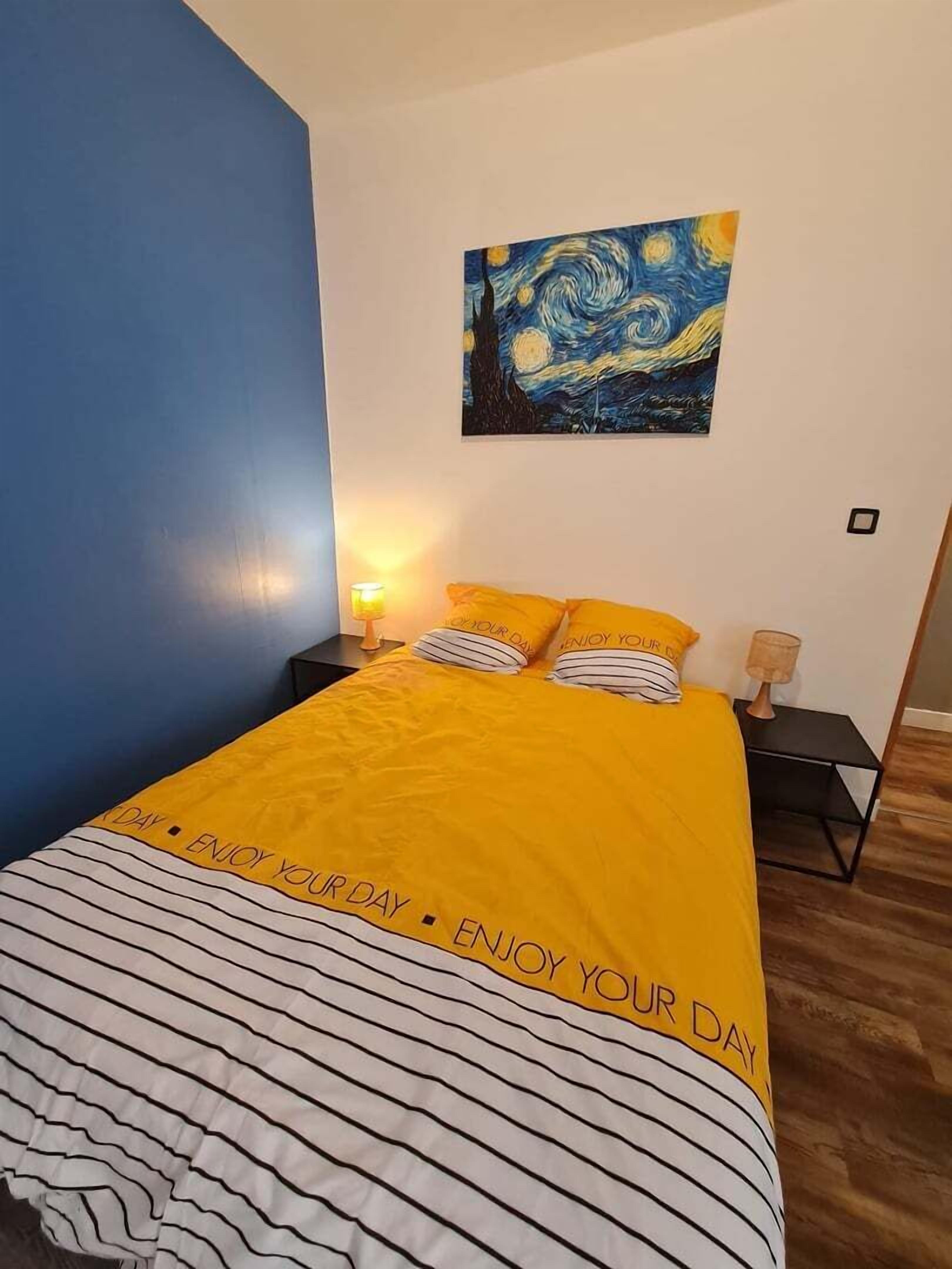 Une chambre à coucher comprenant un lit, deux tables de chevet, une commode, un tableau mural et une lampe.