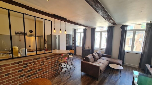 A modern living room with a brick accent wall, a sofa, a small round table, and a dining area with a bar counter.